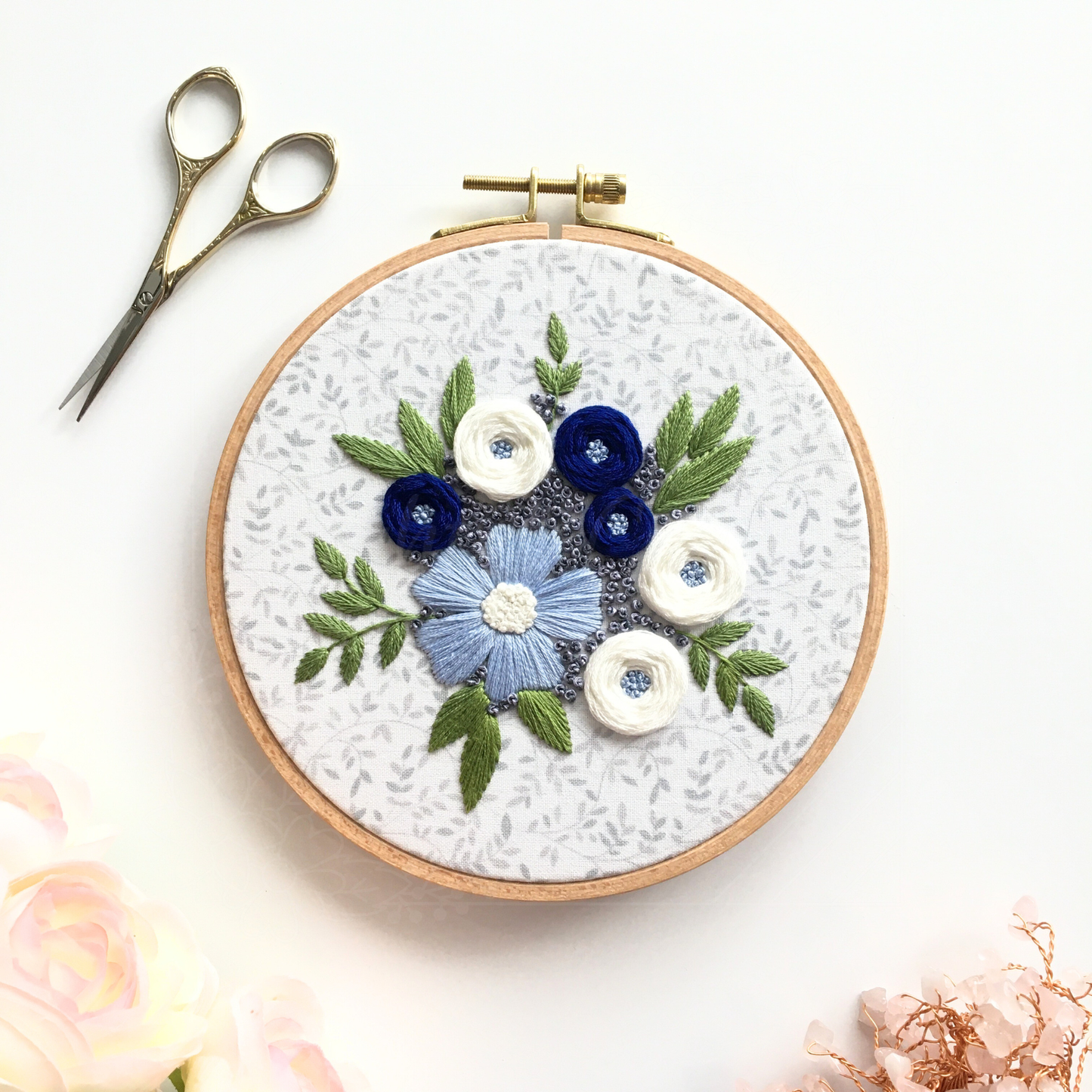 Stitched embroidery design "Winter Blooms" by Eight22Crafts displayed in a round hoop alongside scissors and embroidery thread on a white background