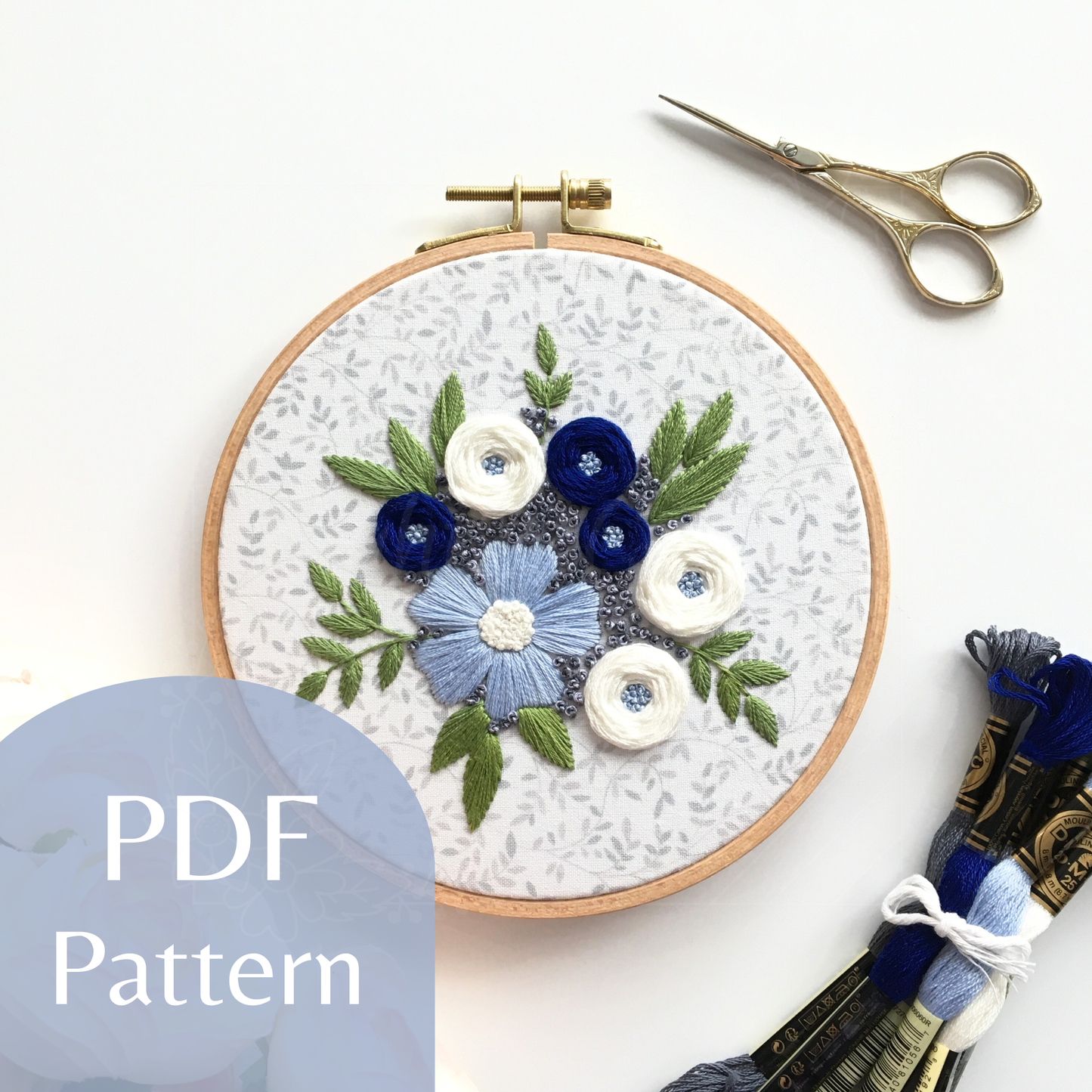 Stitched embroidery design "Winter Blooms" by Eight22Crafts displayed in a round hoop alongside scissors and embroidery thread on a white background
